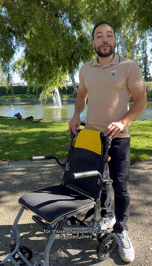 Man holding a wheelchair with a yellow seat in a park setting