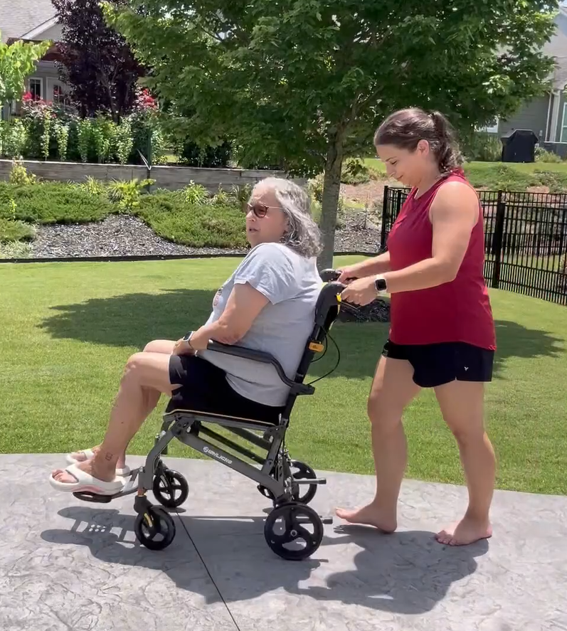 Woman assisting mom in a wheelchair outdoors on a sunny day.